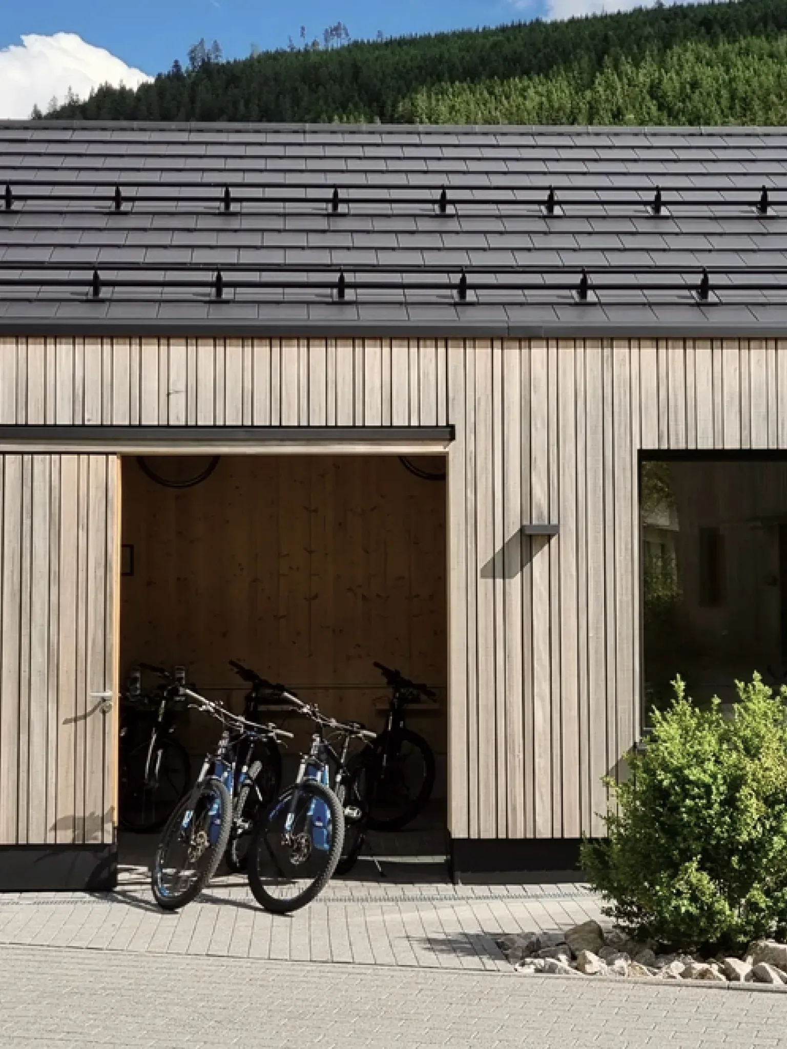 Modernes Holzgebäude mit offenem Tor, darin abgestellte E-Bikes.