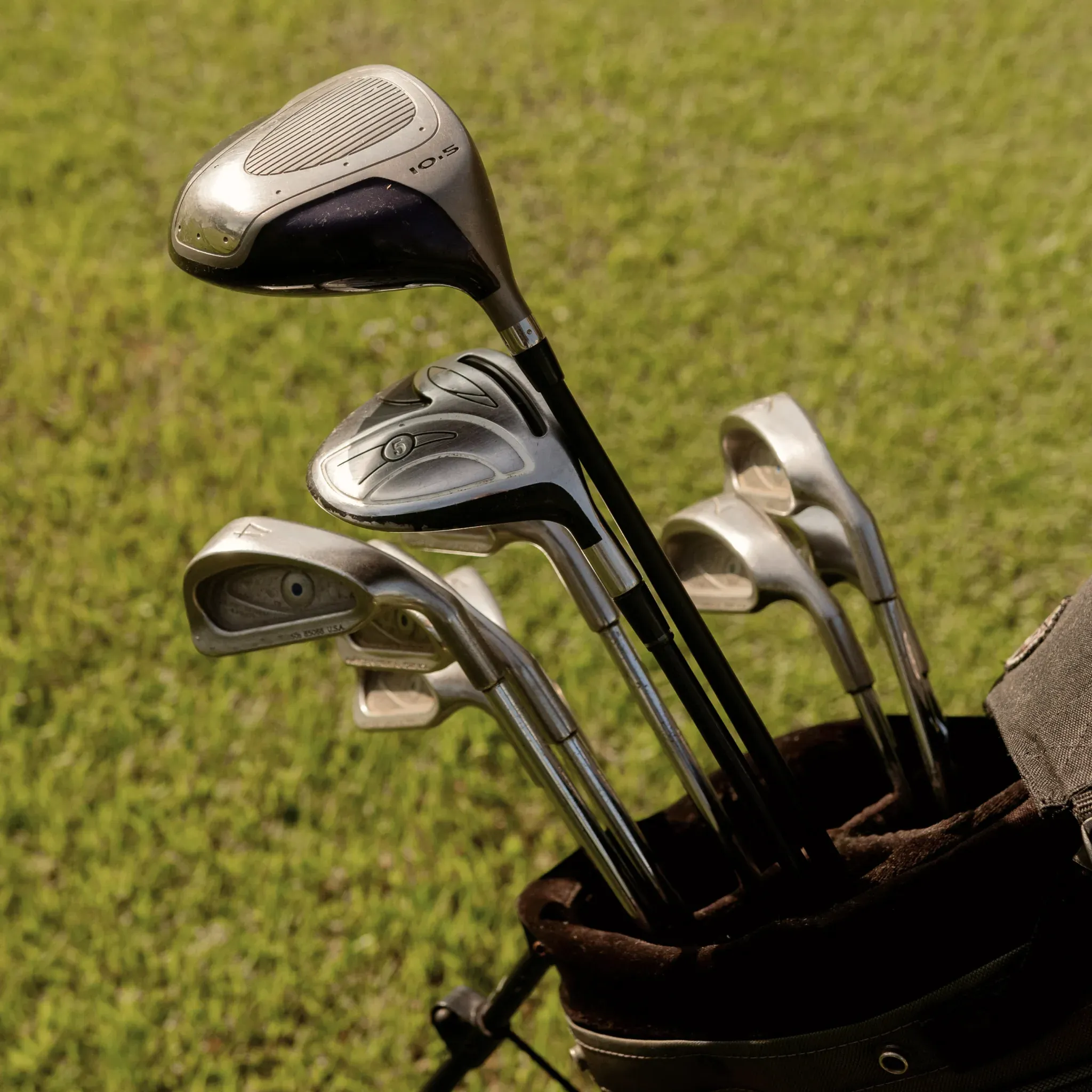 Mehrere Eisen stecken in einem Golfbag auf der Wiese.