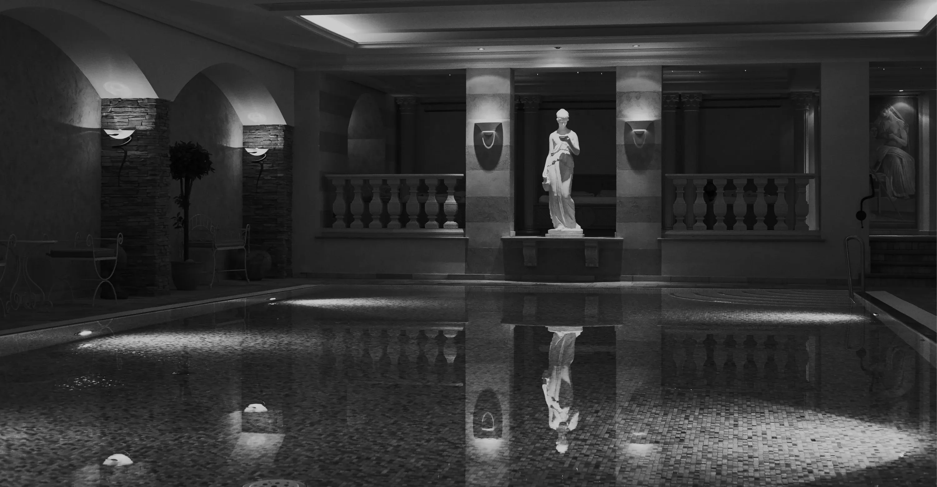 Hallenbad mit Säulen, Statue und spiegelglatter Wasserfläche, Schwarz-Weiß-Aufnahme
