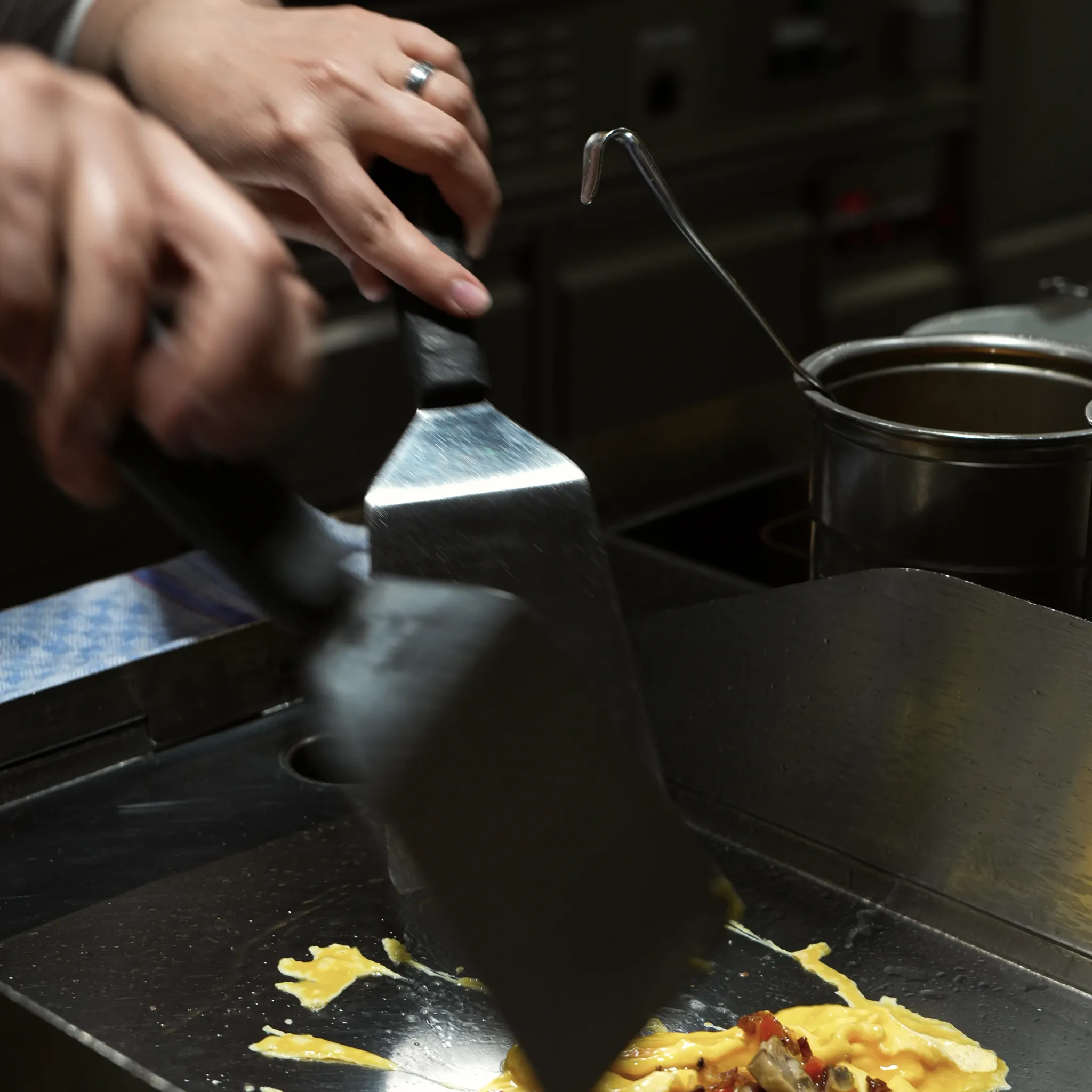 Hand mit Grillschaber auf einer heißen Grillplatte in der Küche.