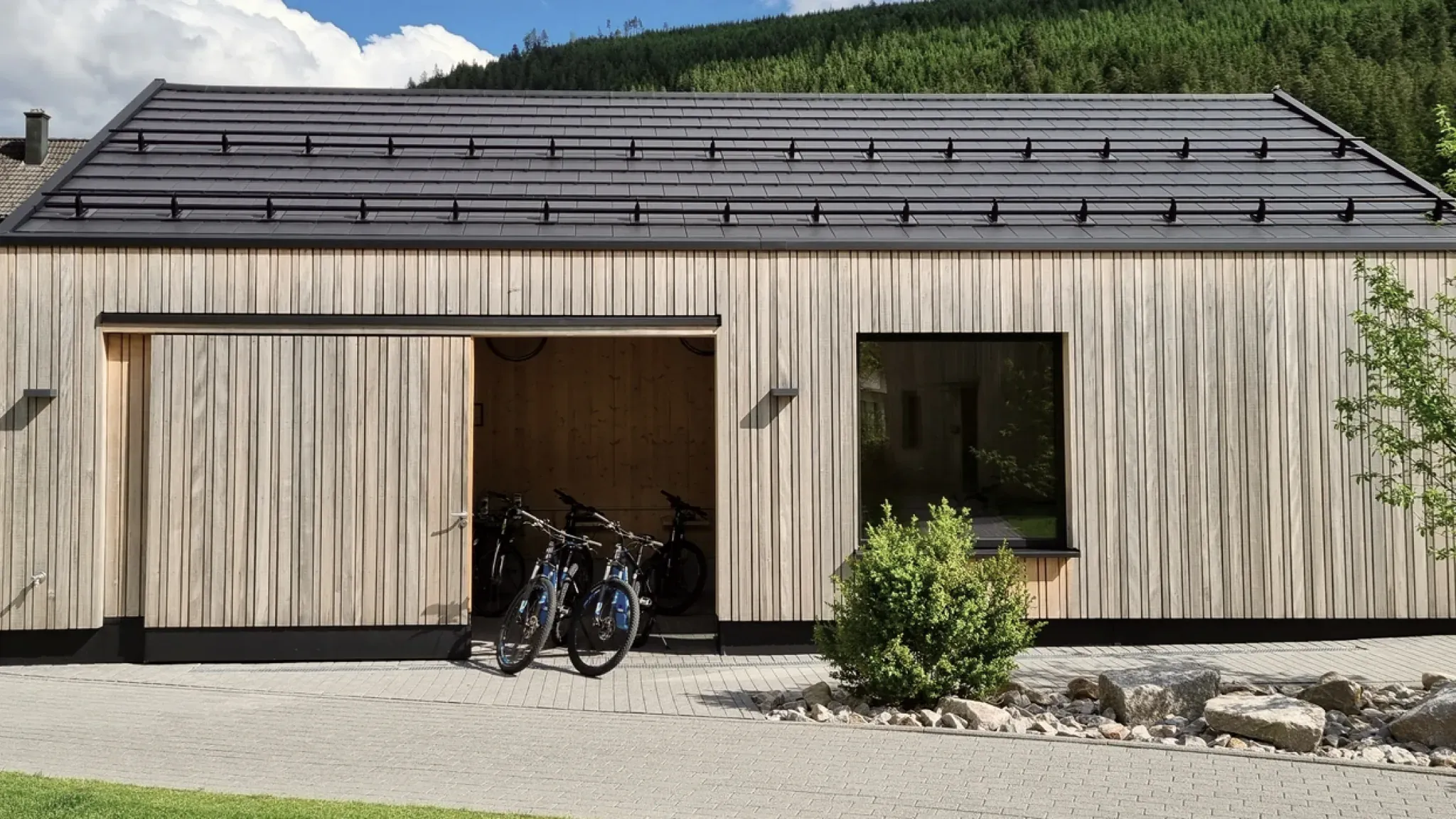 Modernes Holzgebäude mit offenem Tor, darin abgestellte E-Bikes.