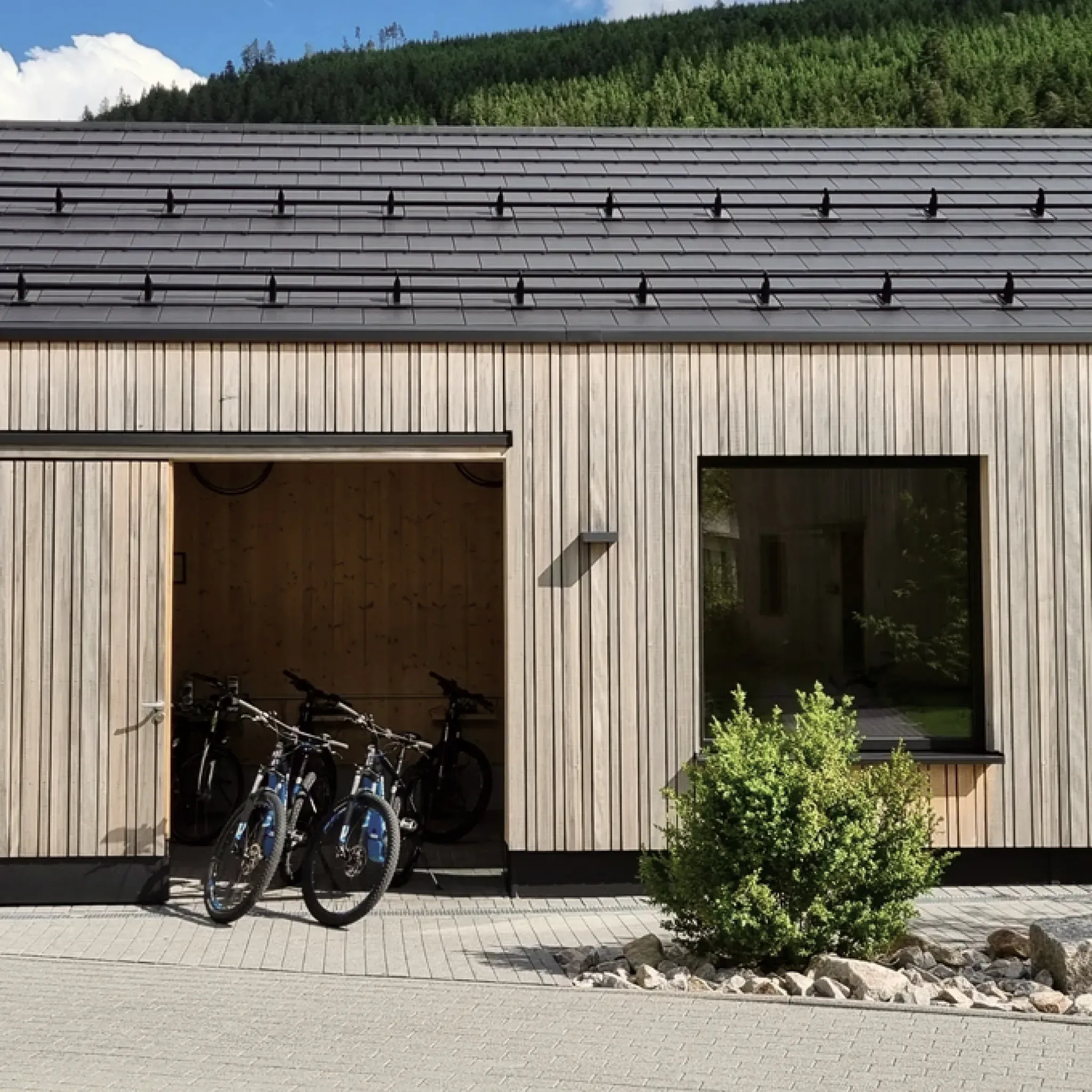 Modernes Holzgebäude mit offenem Tor, darin abgestellte E-Bikes.
