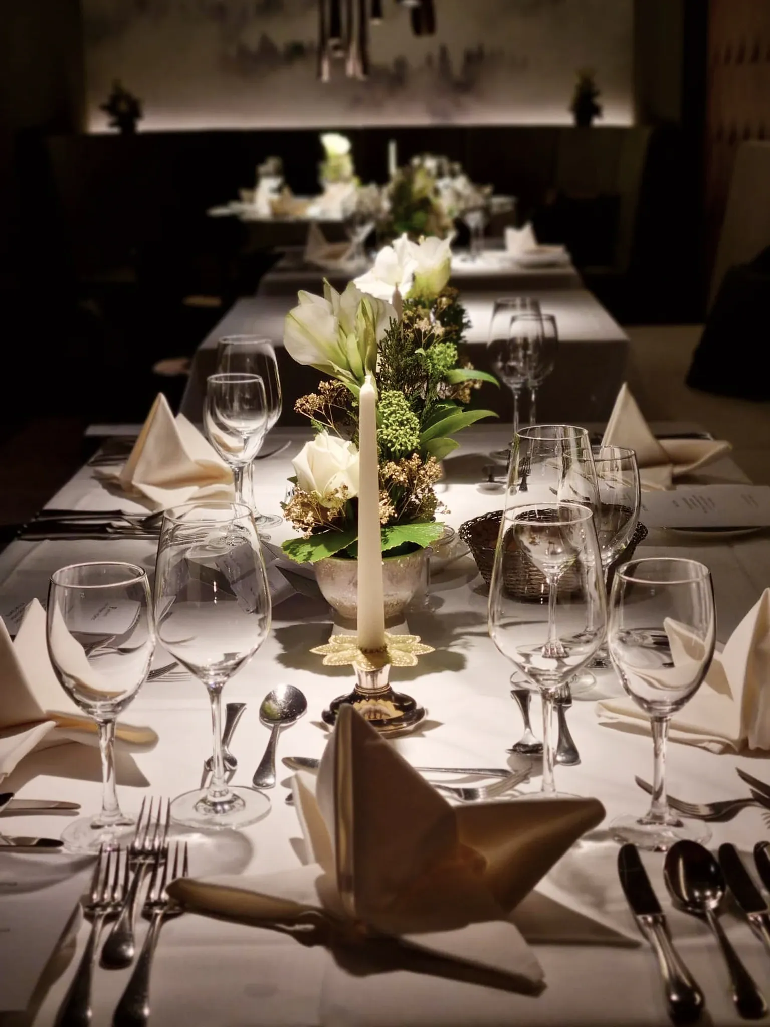 Lange festlich eingedeckte Tafel mit Kerzenleuchter, Blumenschmuck und Kristallgläsern.