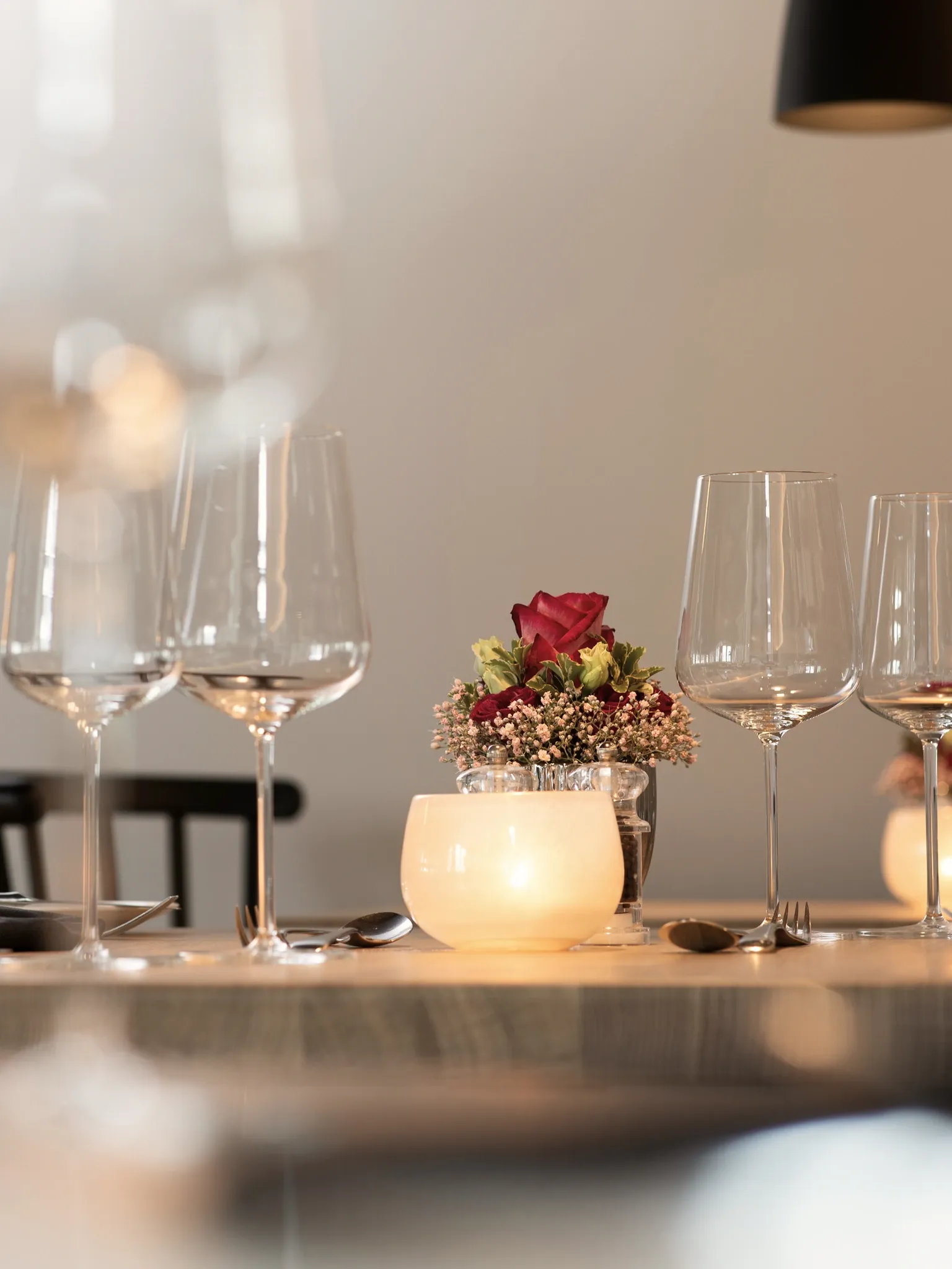 Reihe von Weingläsern auf einer Tischkante mit Teelicht und kleinem Blumenschmuck.