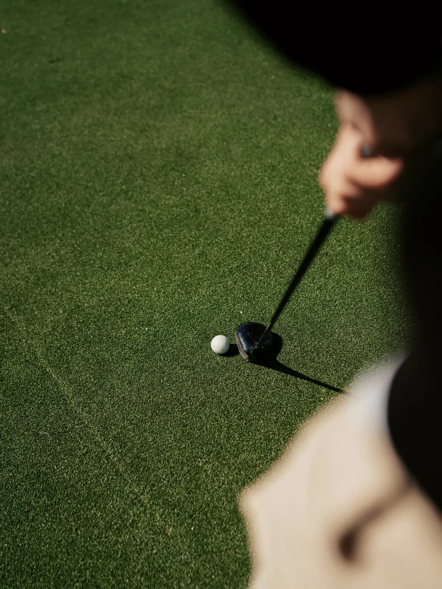 Golfball liegt neben einem Driver-Schlägerkopf auf kurz geschnittenem Rasen.