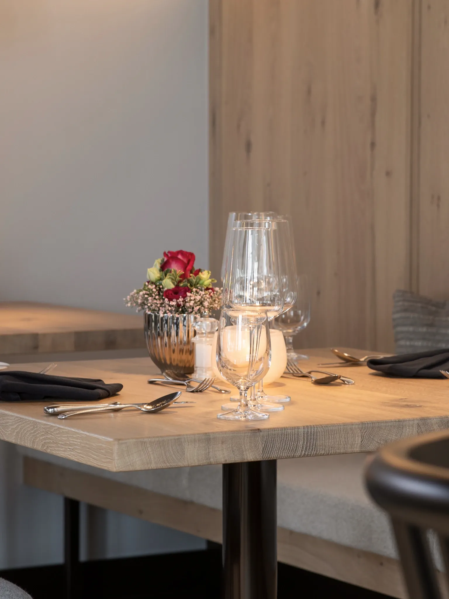 Eingedeckter Holztisch mit kleiner Blumenvase, Weingläsern und Teelicht.