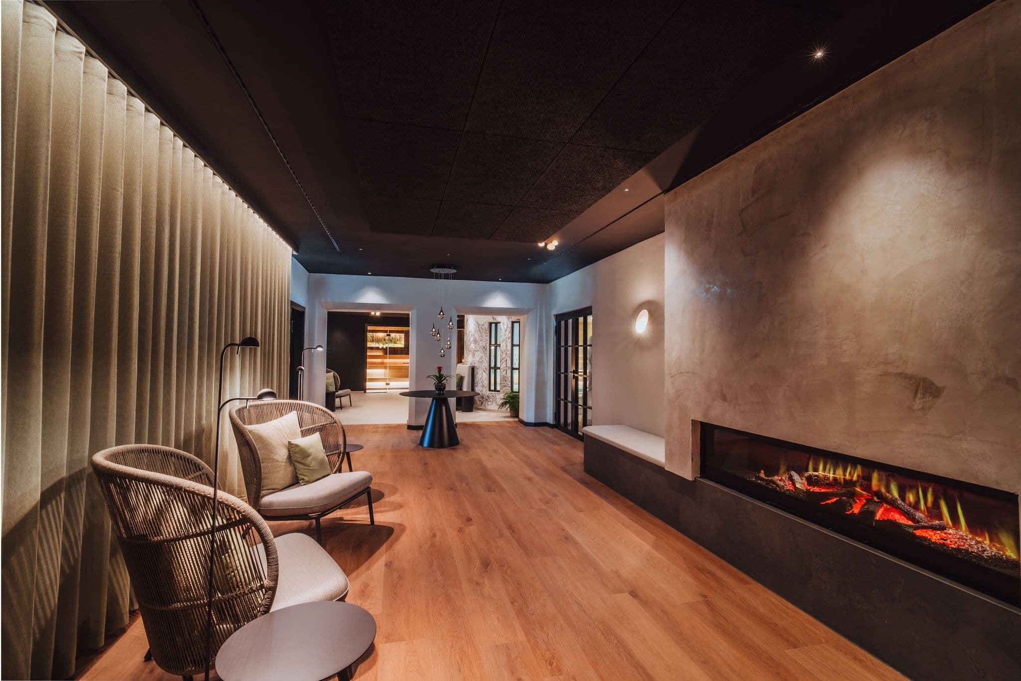 Langer Ruheraum mit Kamin, Vorhang, Korbsesseln und Blick zur Lounge