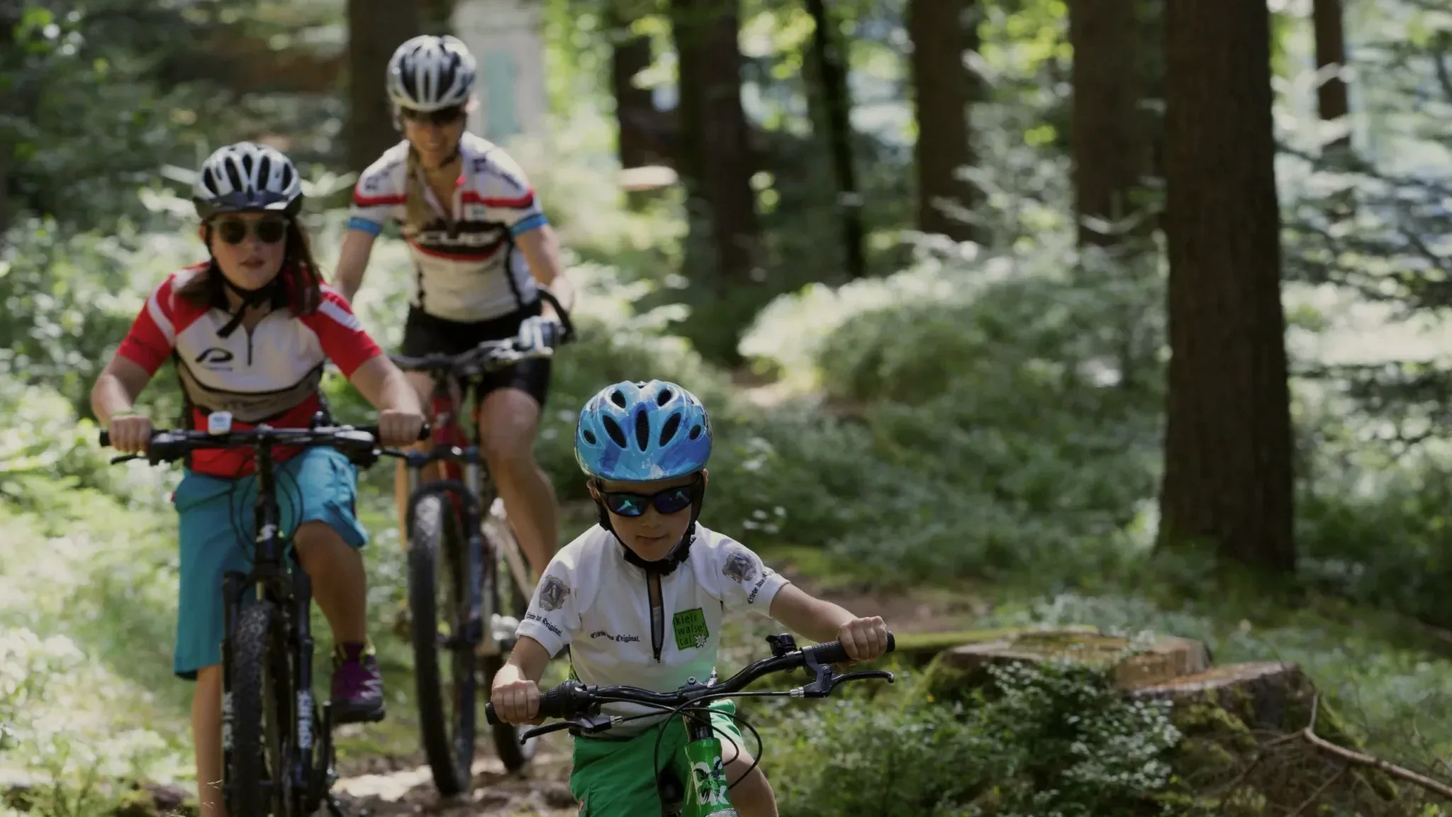 Zwei Kinder und eine Frau fahren mit Mountainbikes über einen Waldweg.