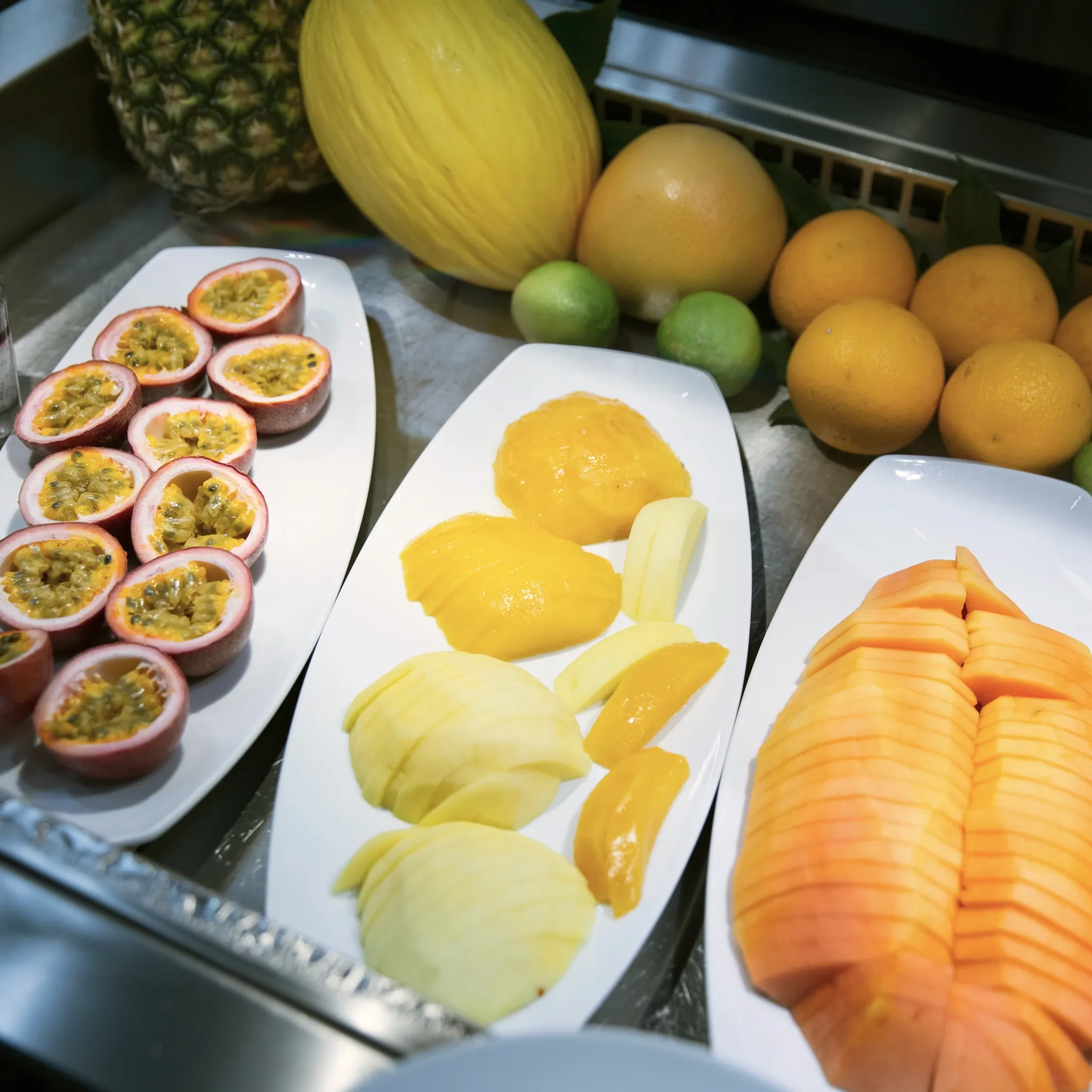 Buffetauslage mit aufgeschnittenen Passionsfrüchten, Melonenspalten, Zitronen und Orangen auf weißen Platten.