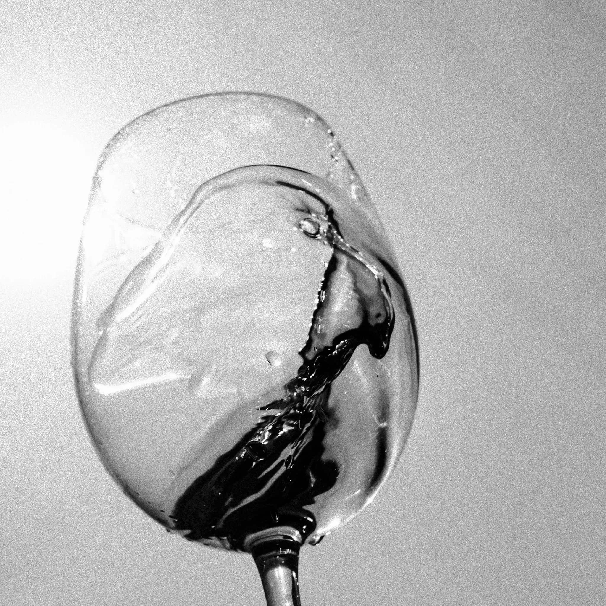 Schwarzweiß-Aufnahme: Rotwein schwappt in einem gekippten Weinglas.