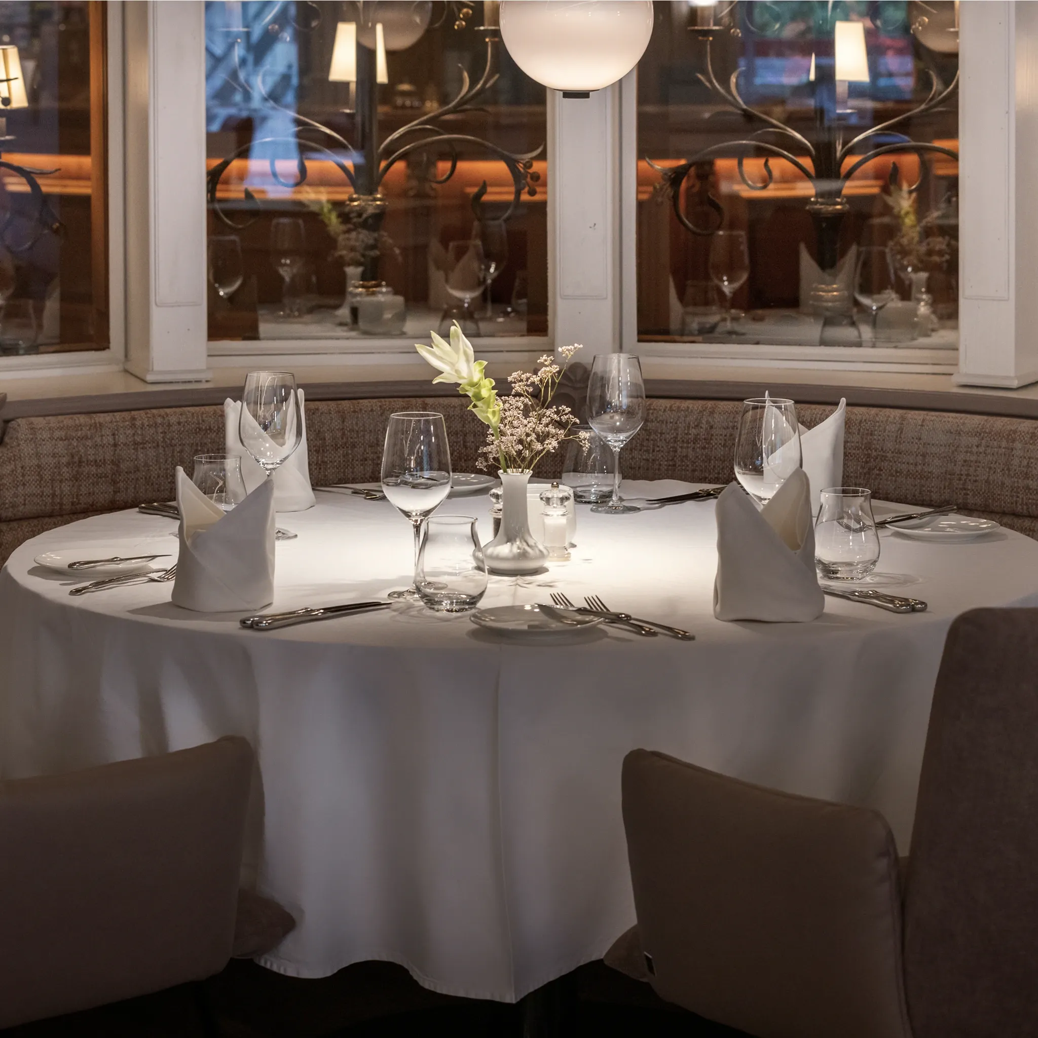 Rund eingedeckter Tisch mit weißer Tischdecke, gefalteten Servietten und Weingläsern in einem klassischen Restaurantsaal.