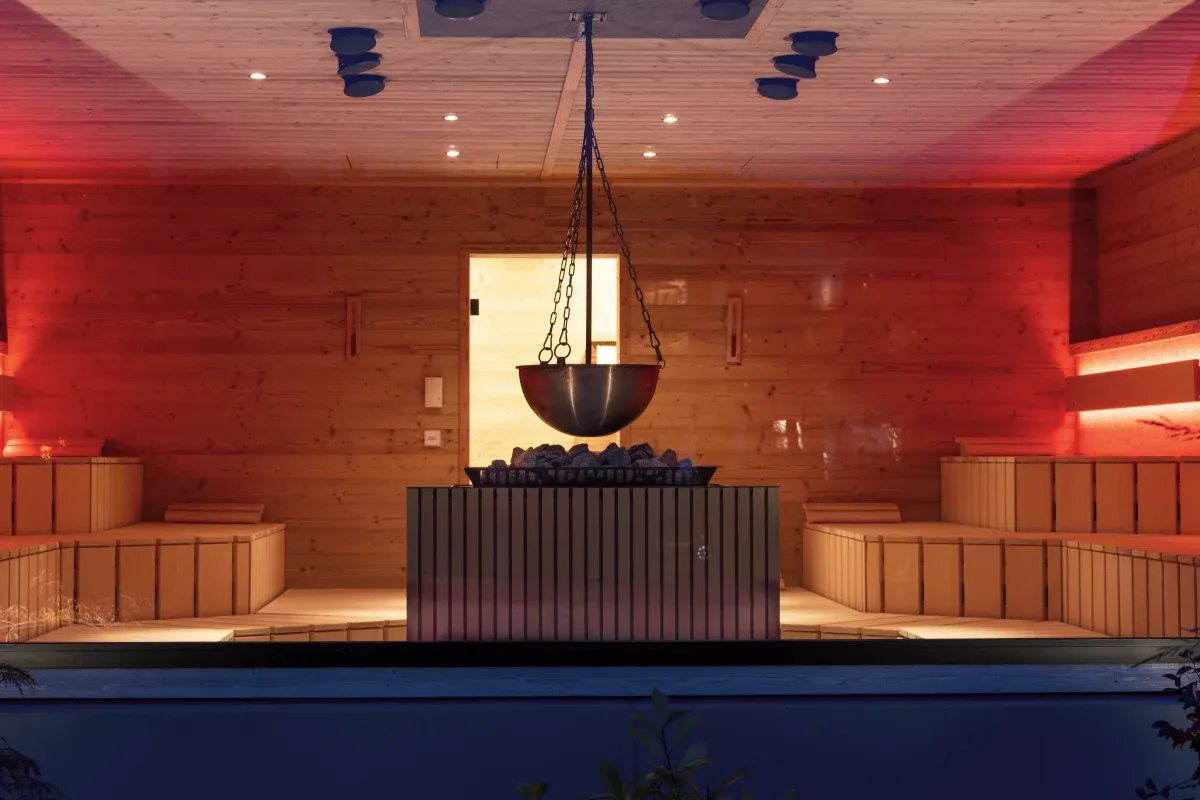 Rot beleuchtete Sauna mit hängendem Aufgusskessel und Holzbänken