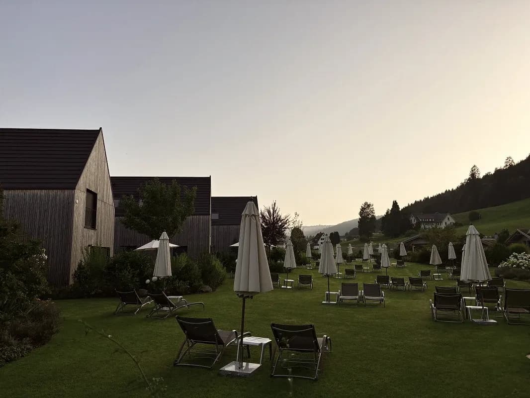 Liegewiese mit Sonnenschirmen und Liegestühlen vor Chalets in der Abenddämmerung