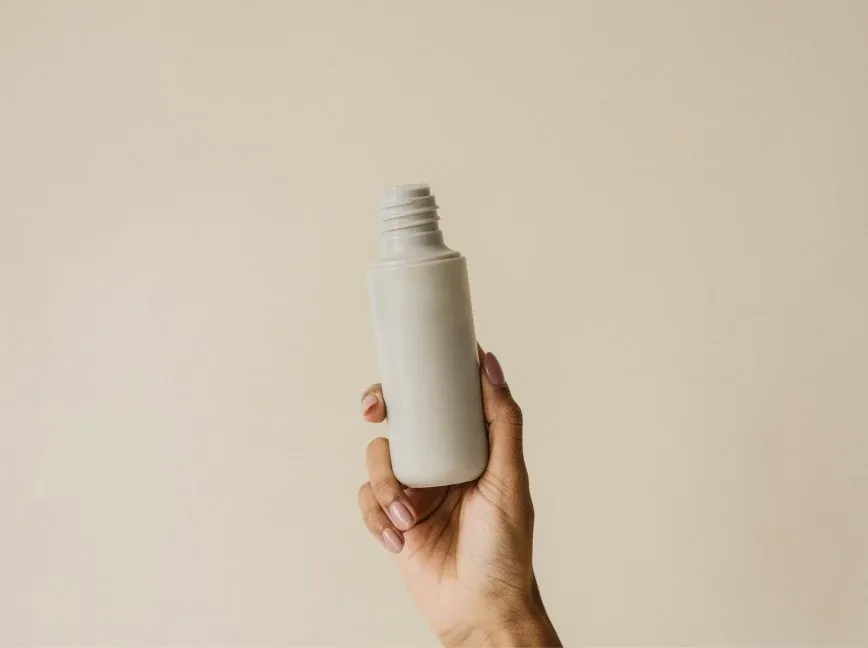 Hand hält eine schlichte weiße Pflegeflasche vor beigem Hintergrund