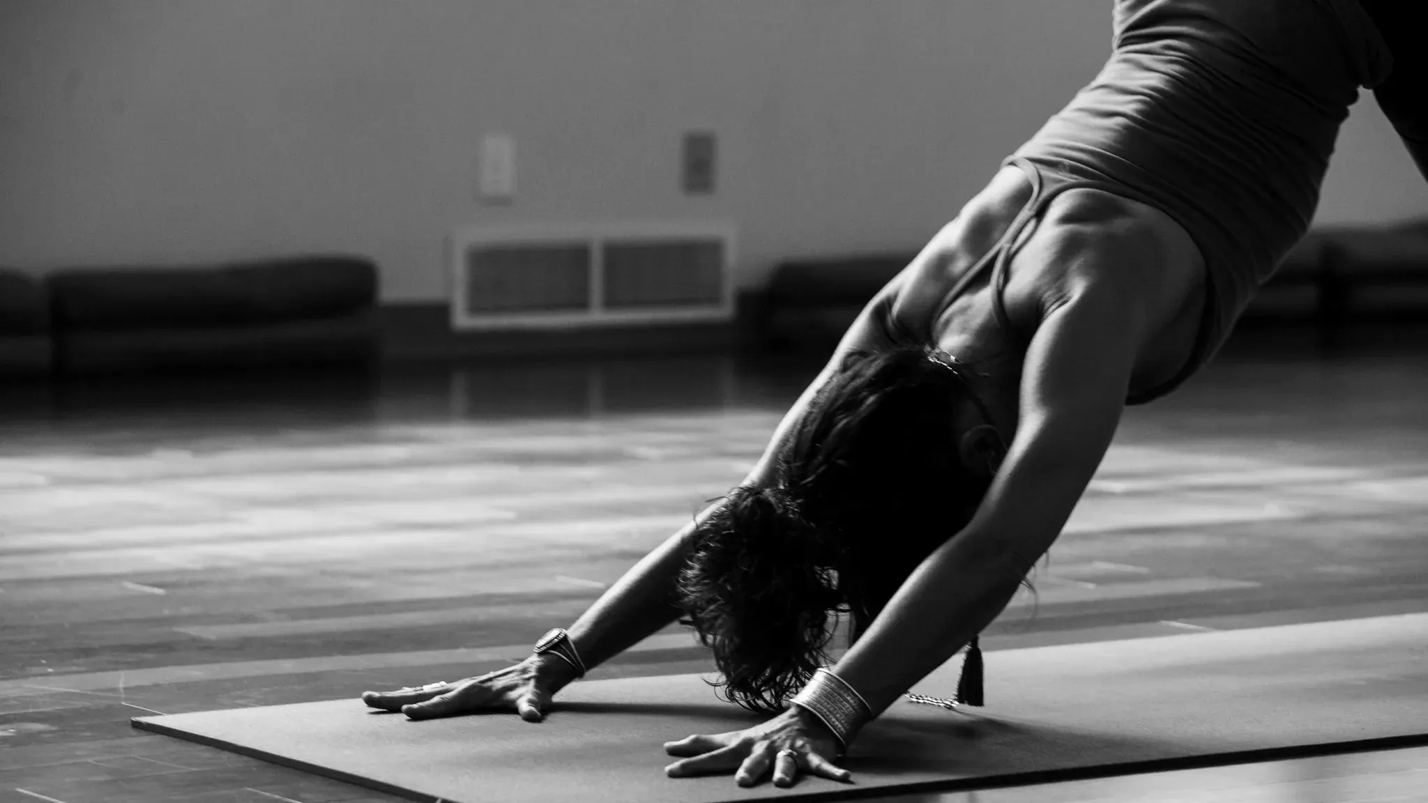 Schwarzweiß-Aufnahme einer Person in der Yoga-Haltung herabschauender Hund auf einer Matte.