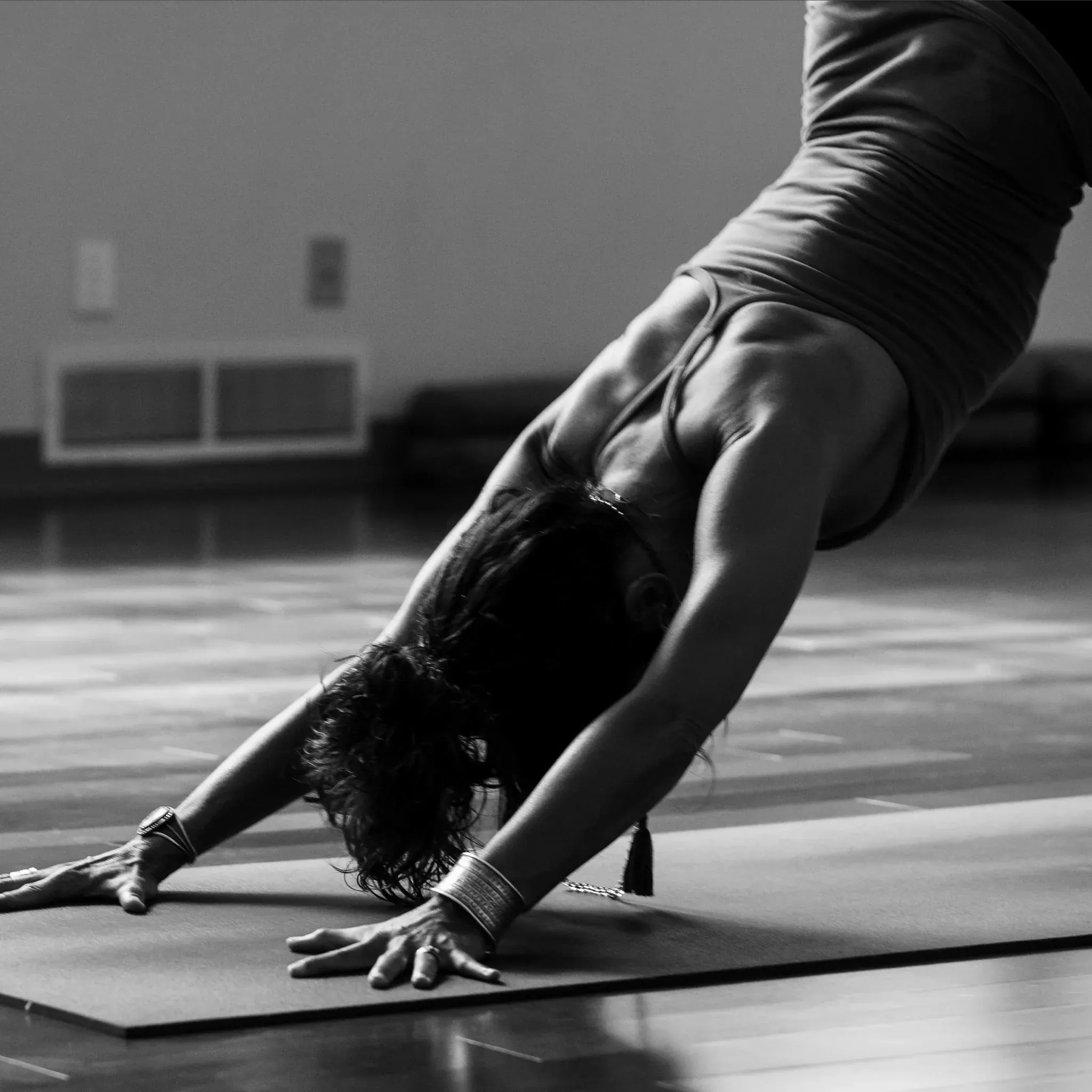 Schwarzweiß-Aufnahme einer Person in der Yoga-Haltung herabschauender Hund auf einer Matte.